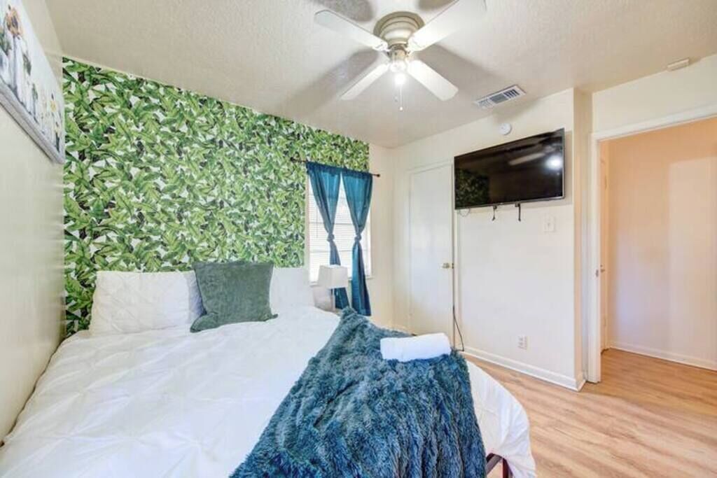 Een slaapkamer met een bed, een plafondventilator, een aan de muur bevestigde televisie en een deur.