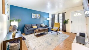 Una sala de estar con una pared azul, un sofá, una mesa de centro, un sillón amarillo y un televisor.