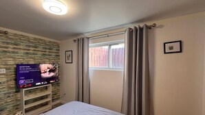 Une chambre à coucher avec un lit, un téléviseur fixé au mur, une fenêtre avec des rideaux et un panneau mural en bois.