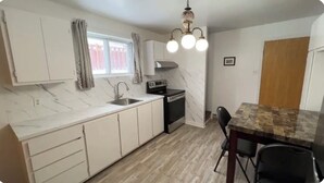Une cuisine avec des meubles blancs, un plan de travail en marbre, une cuisinière et une table à manger avec des chaises.