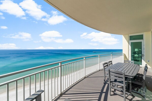 A balcony with a view of the ocean, a table, and chairs.