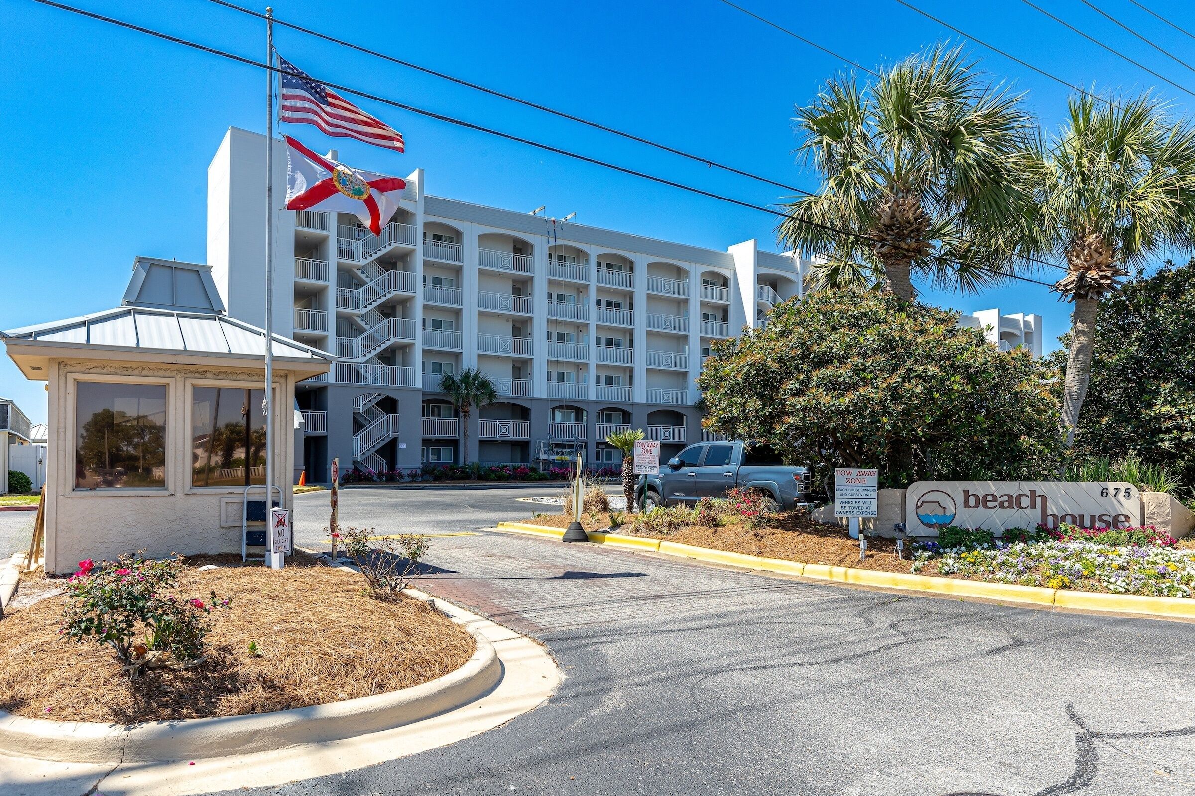 A multi-story hotel with a beach house sign, a no parking sign, and a tow away zone sign.