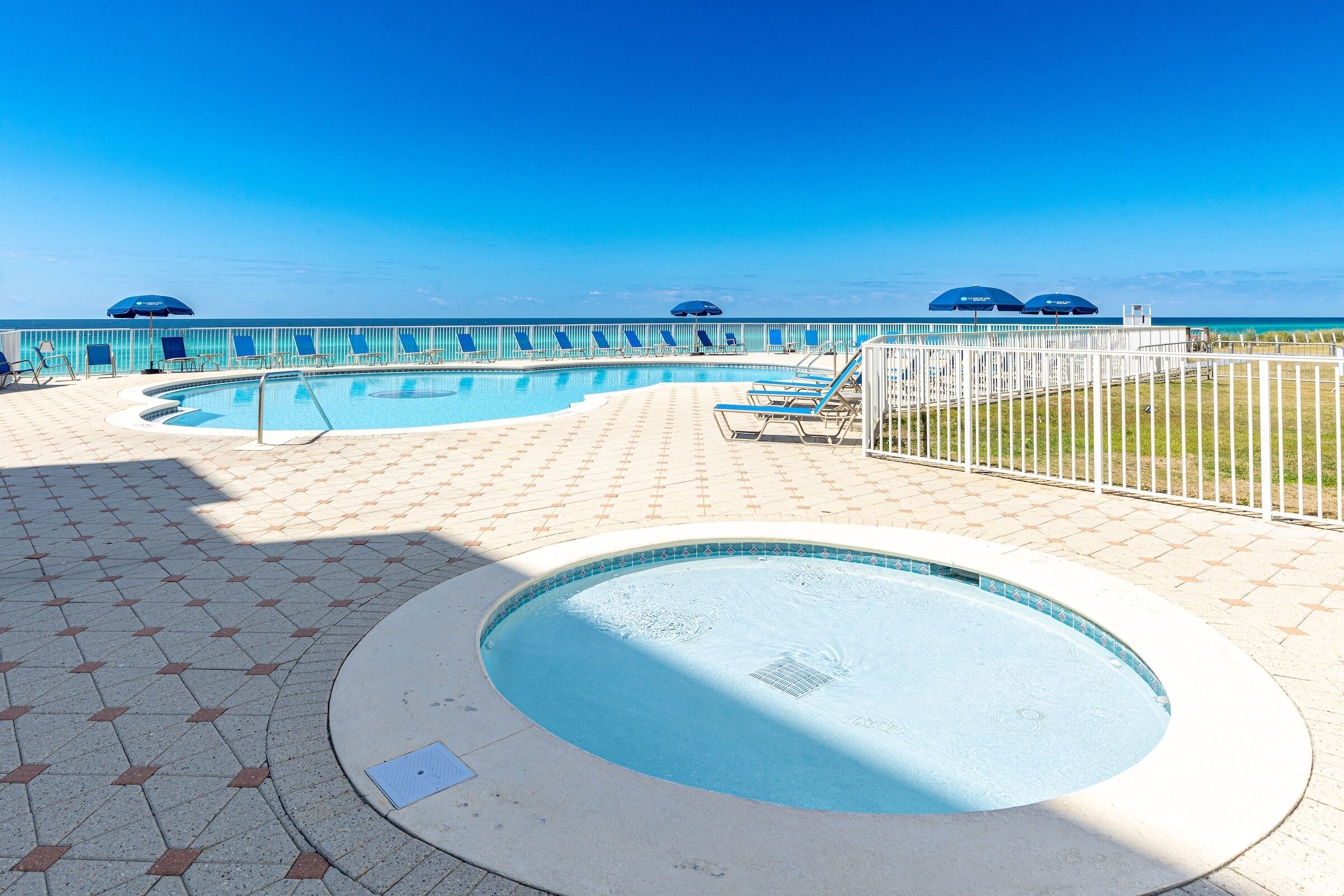 Ein Poolbereich mit Whirlpool, Liegestühlen und Sonnenschirmen mit Blick auf einen Strand.