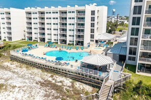 A multi-story hotel with a swimming pool, outdoor seating, and a beach area.