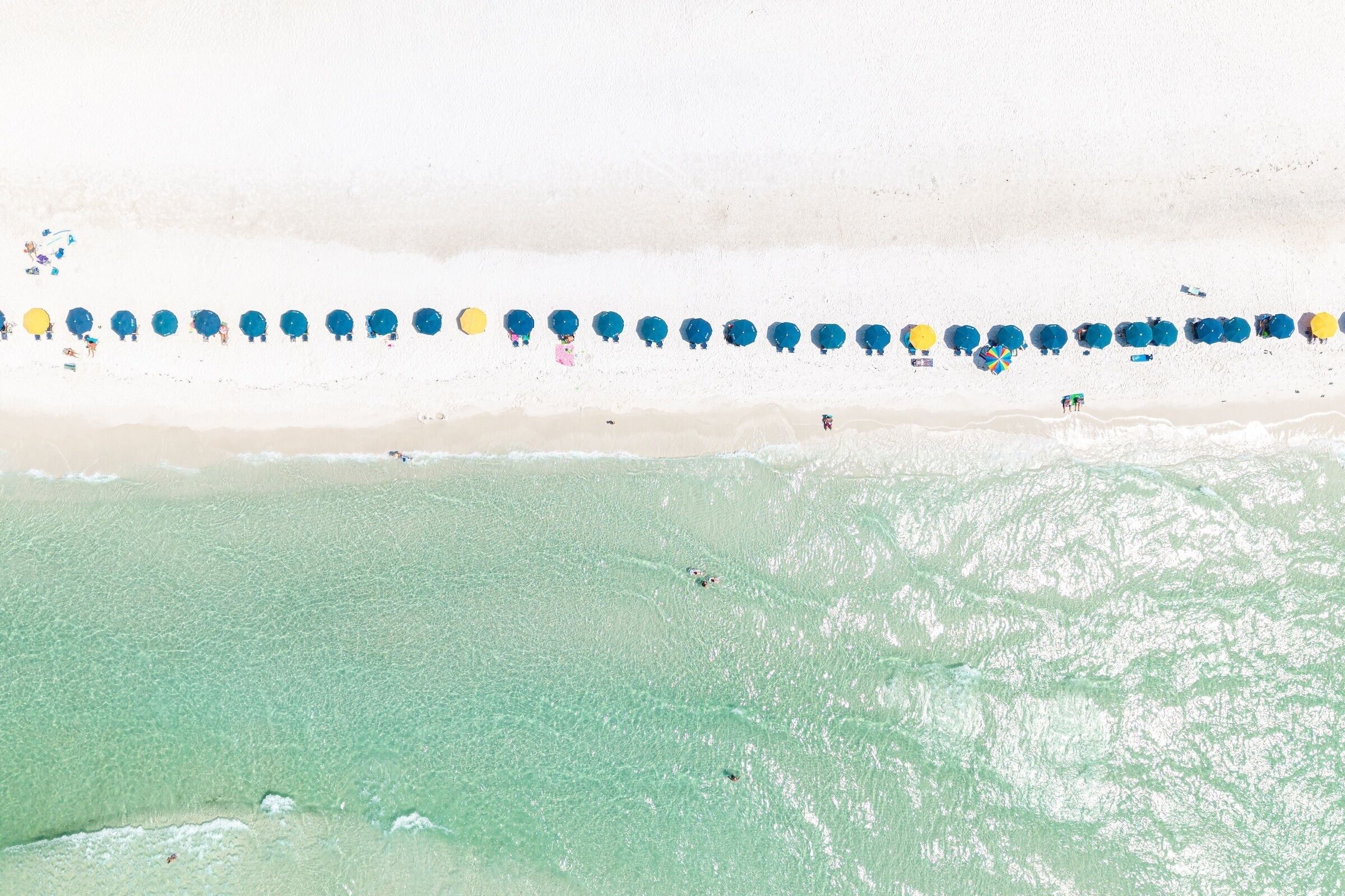 A beach with a row of umbrellas and beachgoers.