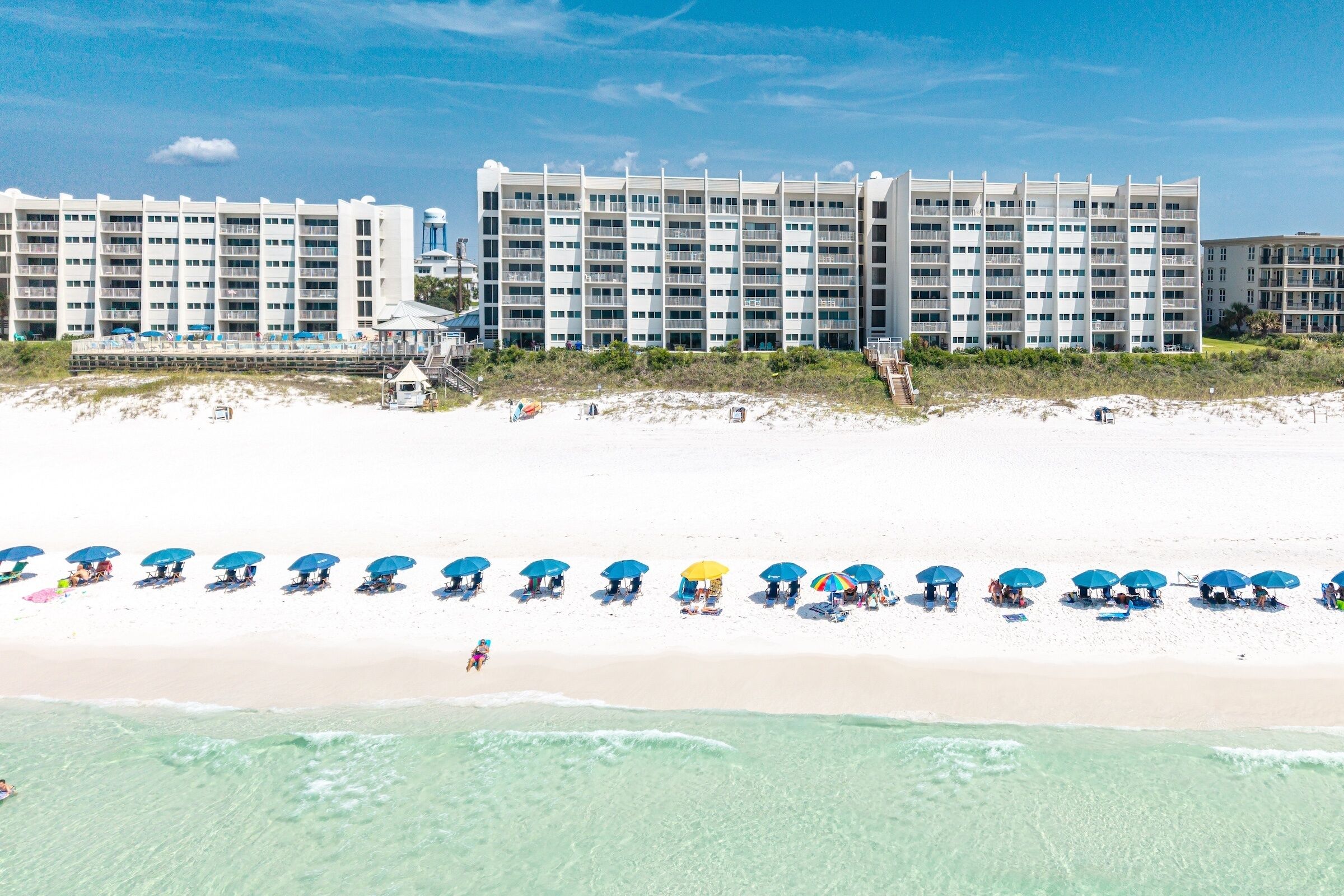 Un hôtel en bord de mer, avec plusieurs étages, une plage de sable et de nombreuses rangées de parasols.