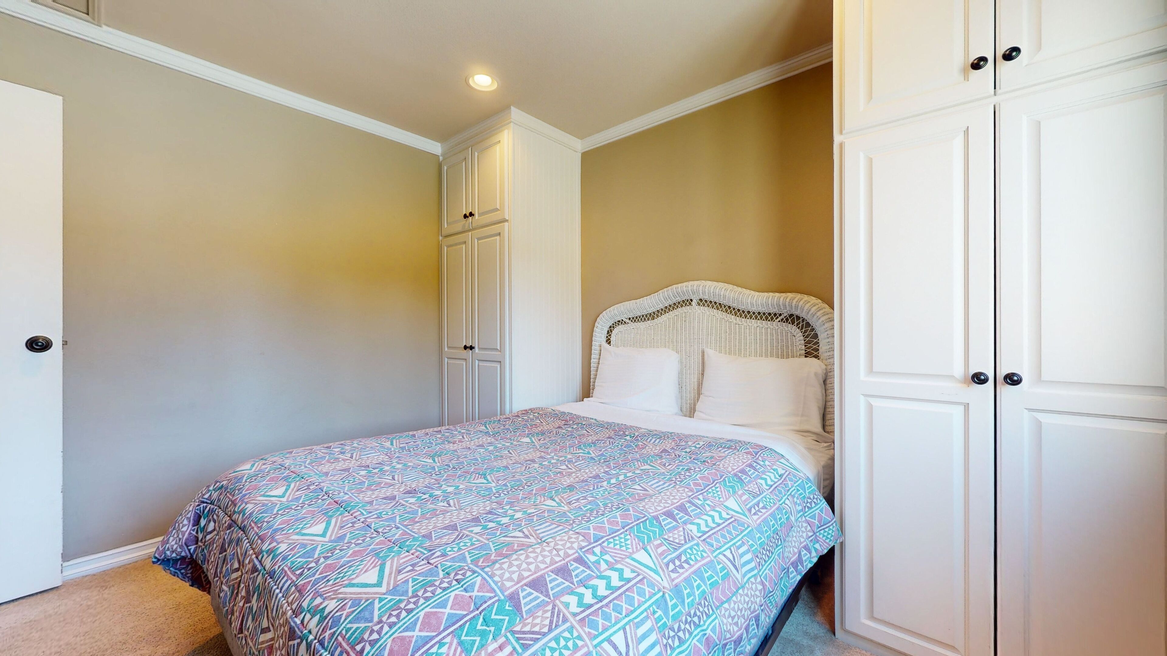 A bedroom with a patterned bedspread, a wicker headboard, and white wardrobes.