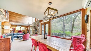 A spacious living area with a wooden dining table, red chairs, and a stone fireplace. - Riverfront Skykomish Cabin w/ Private Hot Tub! (Skykomish)