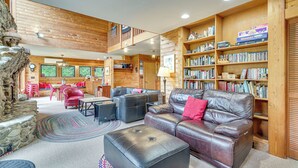 A cozy living room with a fireplace, leather sofas, and a bookshelf filled with books. - Riverfront Skykomish Cabin w/ Private Hot Tub! (Skykomish)