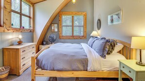 A bedroom with a sloped ceiling, wooden bed frame, and a large window. - Riverfront Skykomish Cabin w/ Private Hot Tub! (Skykomish)