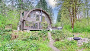 A cabin with a curved roof, surrounded by dense forest. - Riverfront Skykomish Cabin w/ Private Hot Tub! (Skykomish)