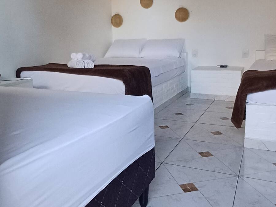 Habitación de hotel con tres camas, ventilador de techo, aire acondicionado y piso de baldosas.