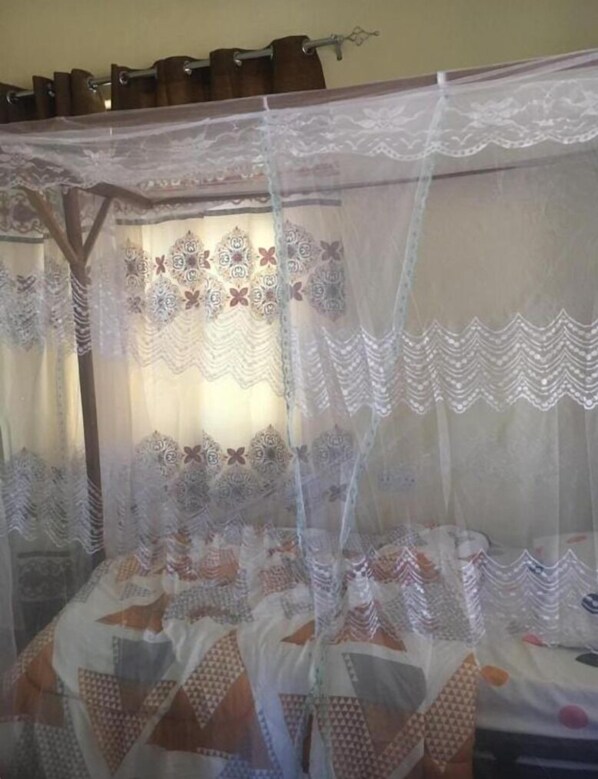 A bed with a patterned bedspread and a canopy with lace detailing. - Rafiki Apartment Hotel (Zanzibar Town)