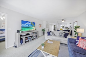 A modern living room with a flat-screen TV, a sofa, a coffee table, and a dining area visible in the background.