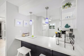 A modern kitchen with a white countertop, hanging pendant lights, and a black backsplash.