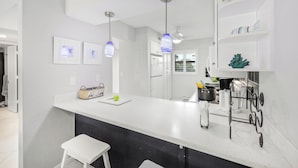 A modern kitchen with a white countertop, hanging pendant lights, and a black backsplash. - Rare Walkout Condo | Pool & Steps to Beach/Food (Marco Island)
