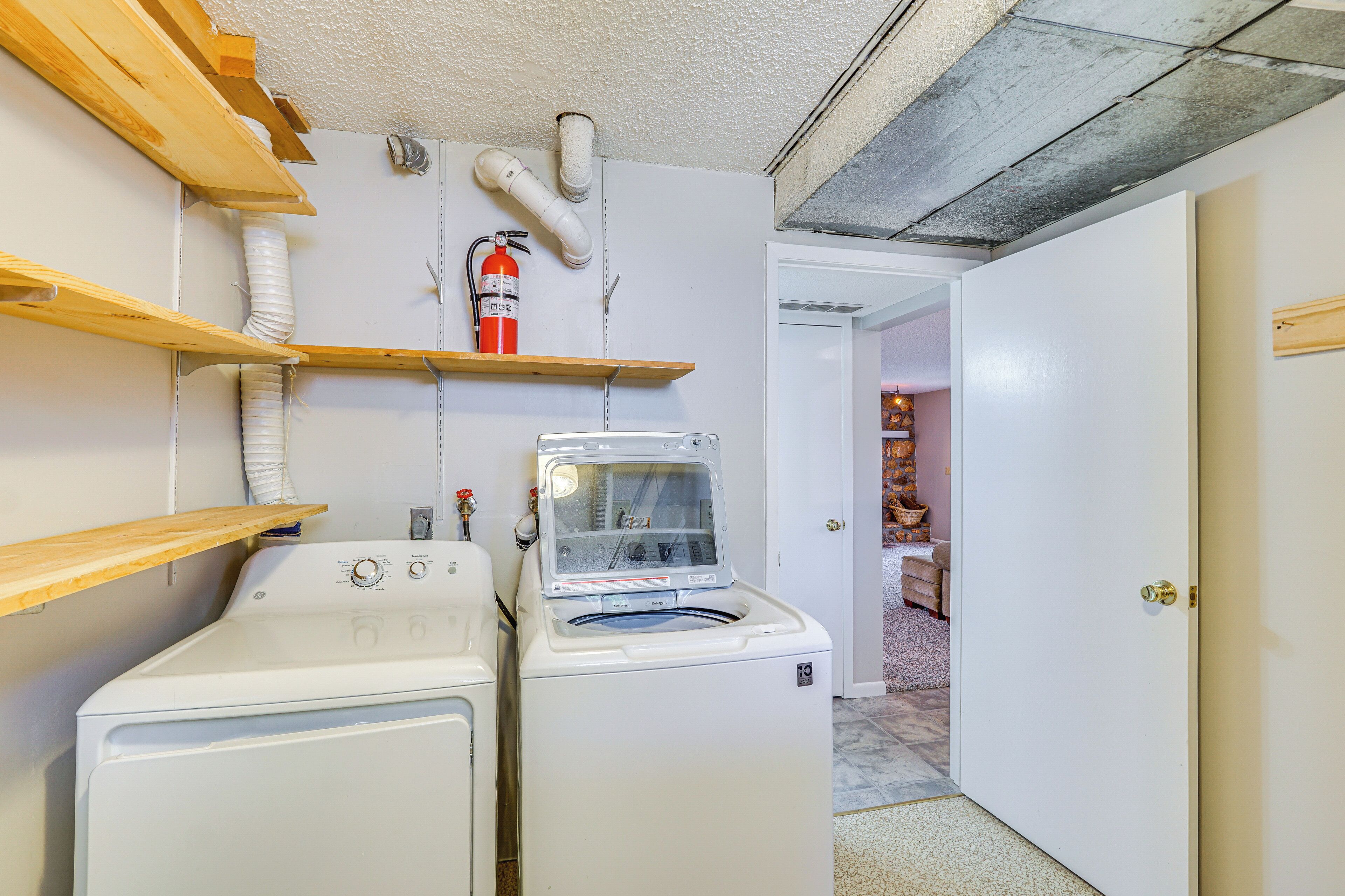 A laundry room with two washing machines, a fire extinguisher, and wooden shelves.