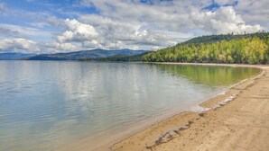 A calm lake with a sandy beach and a forested hillside in the background. - Beachfront Sagle Retreat w/ Boat Dock & Lift (Sagle)