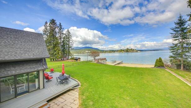 A modern house with a deck overlooking a lake, featuring a patio with outdoor furniture and a view of the water. - Beachfront Sagle Retreat w/ Boat Dock & Lift (Sagle)