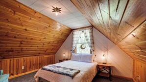 A cozy attic bedroom with wooden walls, a large bed, two bedside lamps, and a window with a moon decoration. - Fire Pit + Community Perks: Murphy Family Cabin! (Murphy)