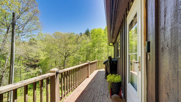 A wooden deck with a railing, a door with a window, and a view of a forested area. - Fire Pit + Community Perks: Murphy Family Cabin! (Murphy)
