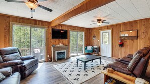 A spacious living room with a fireplace, leather sofas, a coffee table, and a ceiling fan. - Fire Pit + Community Perks: Murphy Family Cabin! (Murphy)