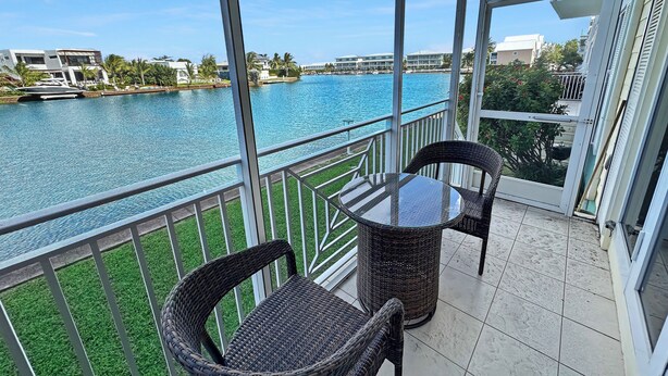 A balcony with a view of a river, wicker chairs, and a glass table. - Cayman Blu 2 Bedroom Waterfront Condo (Grand Harbour)