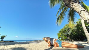 A beach with a large statue of a sea creature lying on the sand, palm trees, and a clear blue sky. - Cayman Blu 2 Bedroom Waterfront Condo (Grand Harbour)