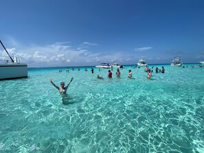 Un mar turquesa transparente con gente nadando y barcos al fondo.
