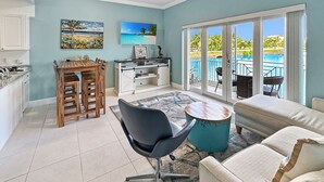 A spacious living area with a dining table, chairs, a sofa, a ceiling fan, and a view of a pool through large sliding doors. - Cayman Blu 2 Bedroom Waterfront Condo (Grand Harbour)