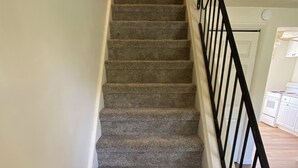 Un escalier recouvert de moquette, avec des rampes noires, menant à l’étage supérieur.
