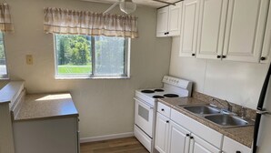 Une cuisine avec des meubles blancs, une cuisinière, un évier et une fenêtre donnant sur un paysage verdoyant.