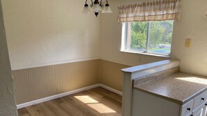 Une cuisine avec un plancher en bois, des meubles blancs et une fenêtre offrant une belle vue, ainsi qu’un luminaire au-dessus du comptoir.
