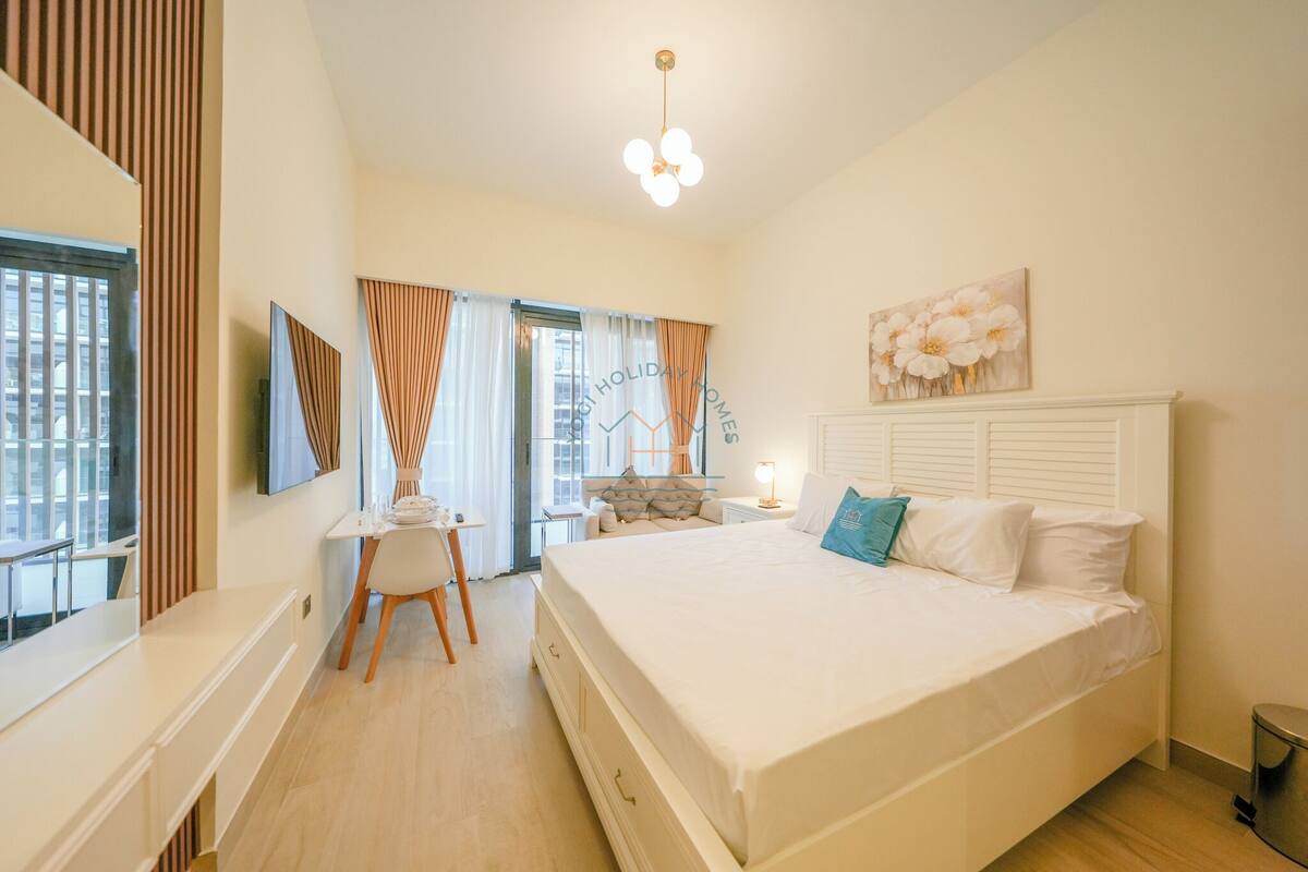 Une chambre moderne avec un lit, un bureau et une chaise. Il y a une fenêtre avec des rideaux, un tableau au mur et un luminaire au plafond.