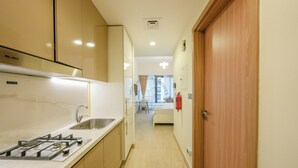 Une cuisine moderne équipée d’une cuisinière à gaz, d’un évier et de meubles en bois. Un couloir mène à une chambre à coucher avec un lit et une fenêtre.