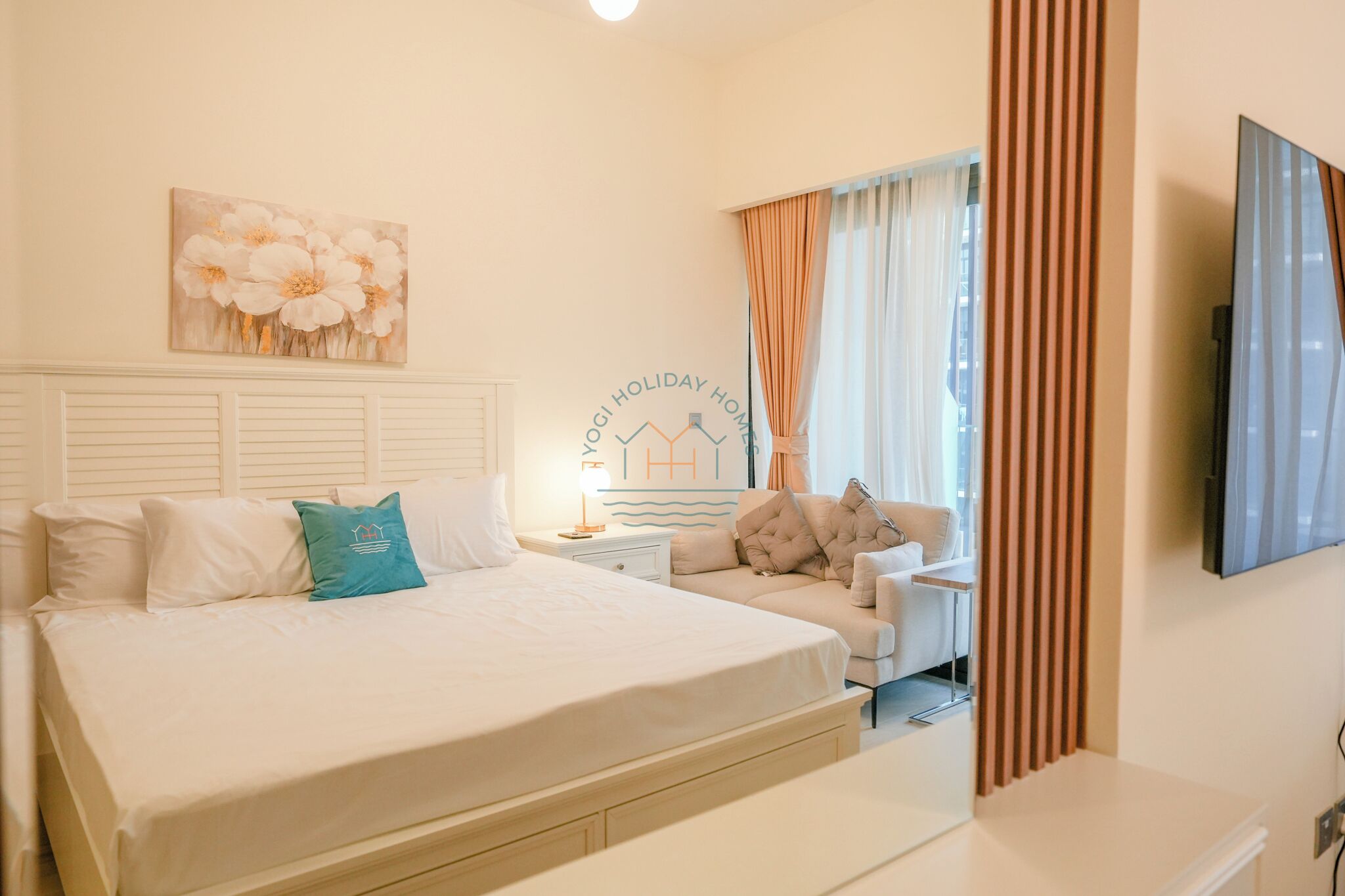 Habitación de hotel con una cama grande, un sofá, un televisor y una pared con un cuadro floral.