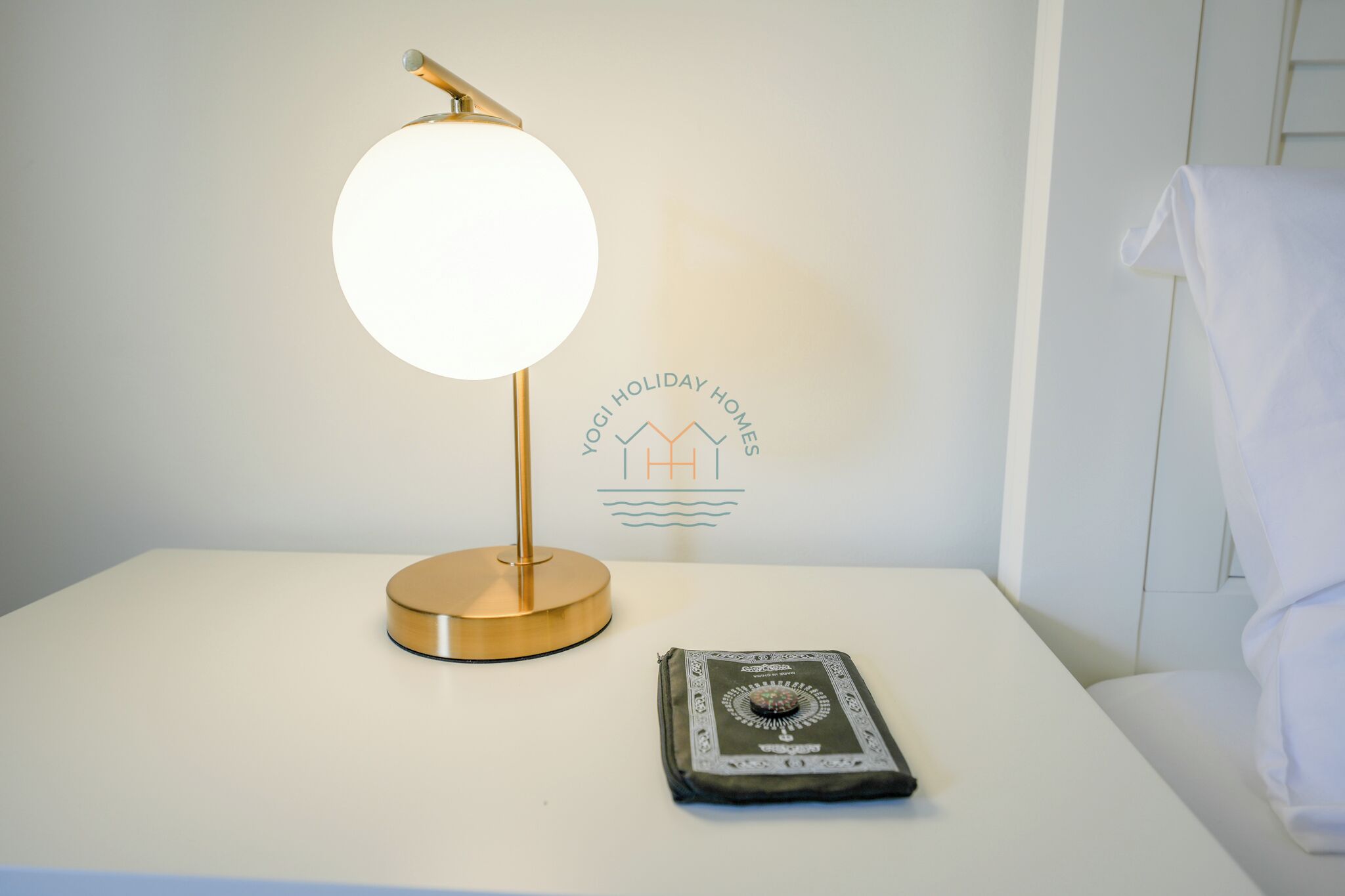 Ein Nachttisch mit Lampe, einer Gebetsmatte und einer Wand mit einem Logo.