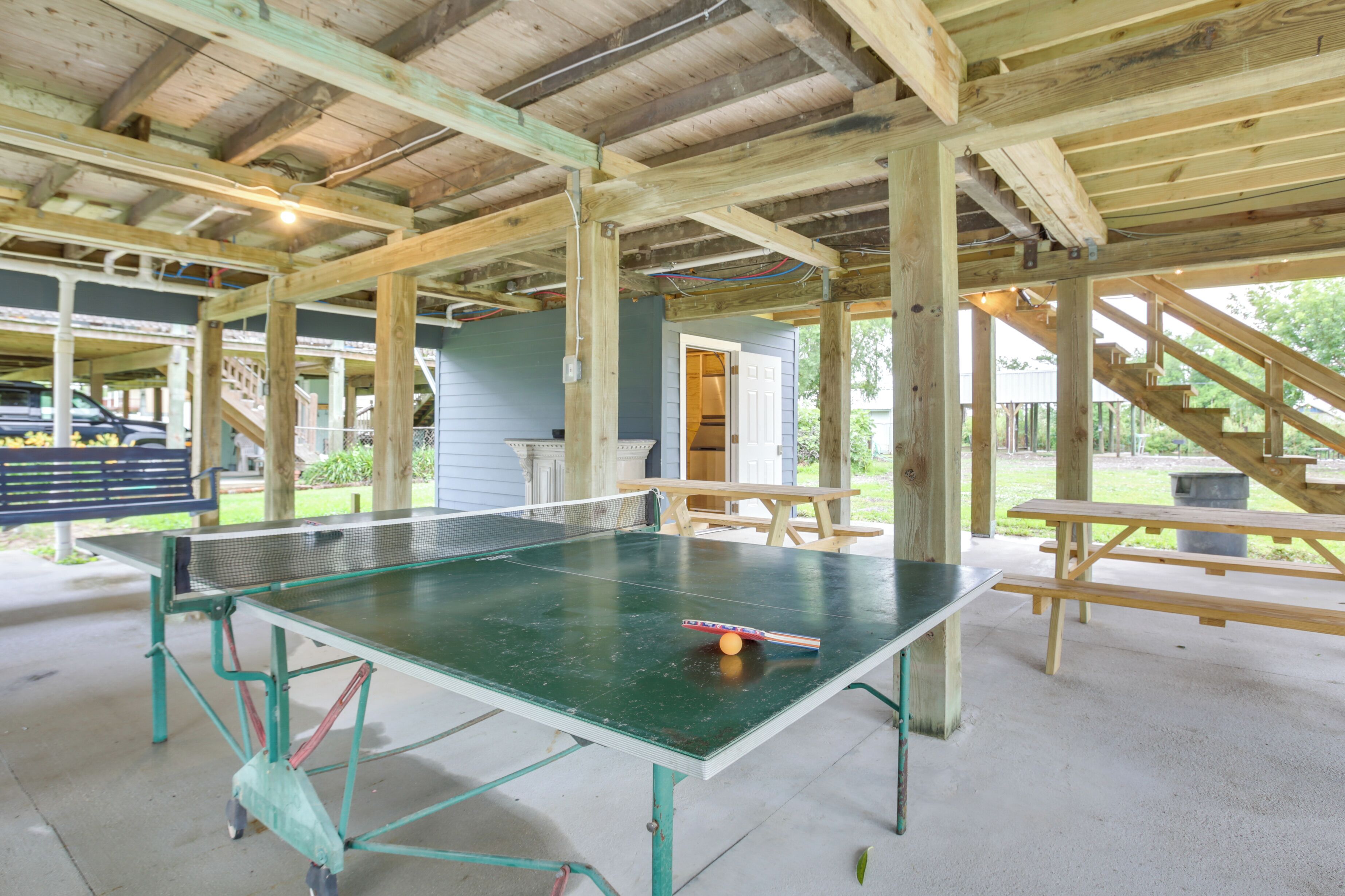 Une table de ping-pong dans un pavillon extérieur doté de poutres en bois et d’un sol en béton.