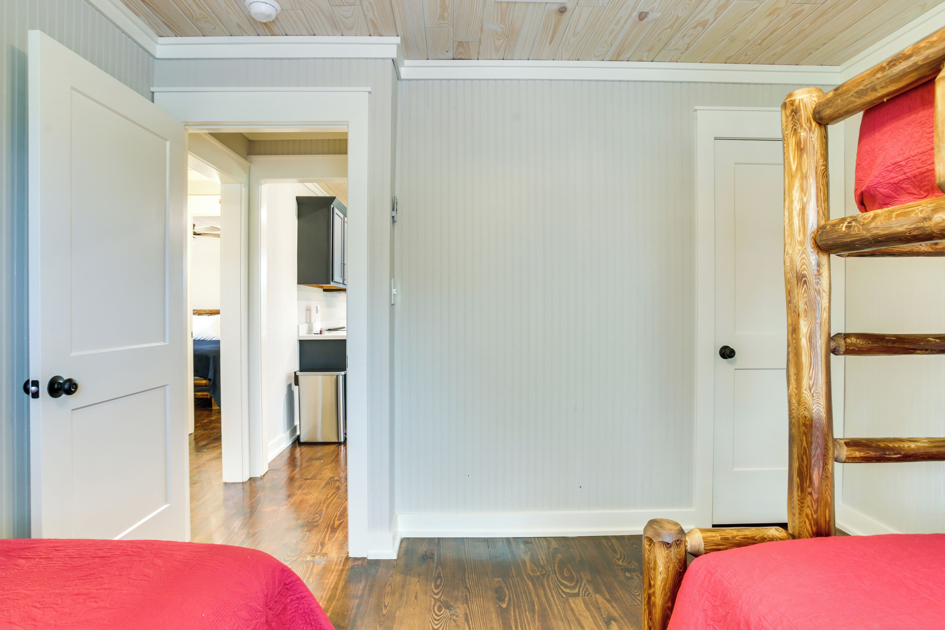 A bedroom with a wooden bed frame, a white door, and a hallway leading to a kitchen.