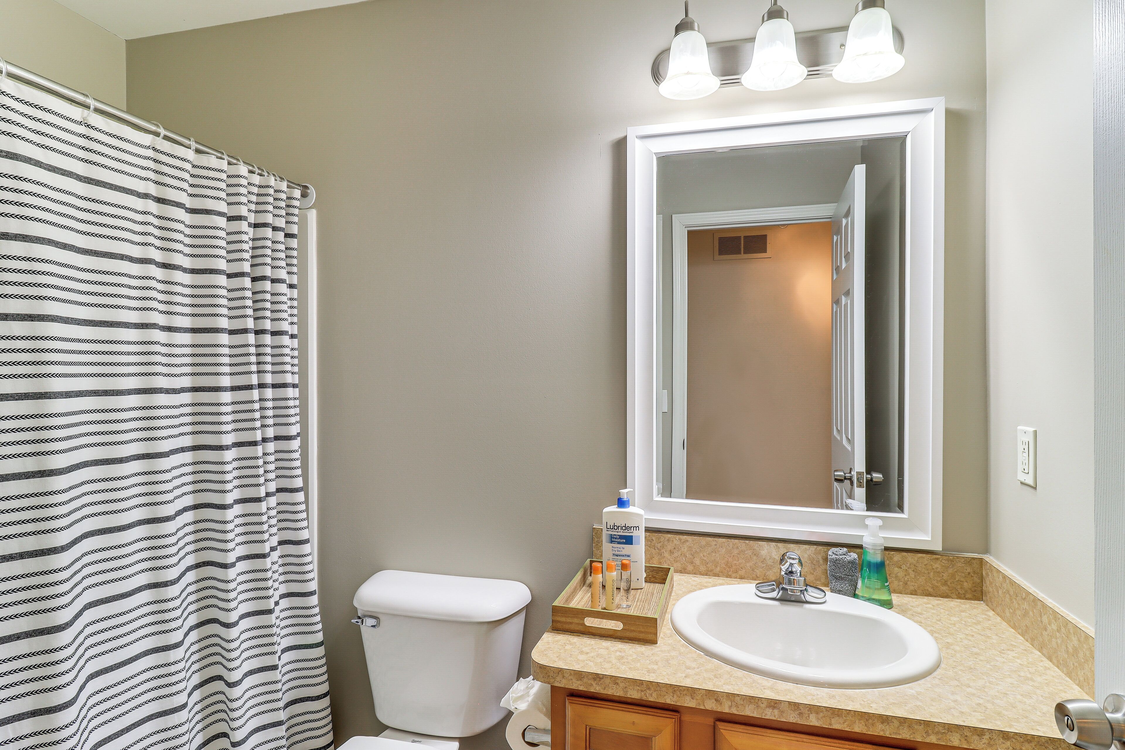 A bathroom with a striped shower curtain, a toilet, a sink with a mirror, and toiletries on the counter.