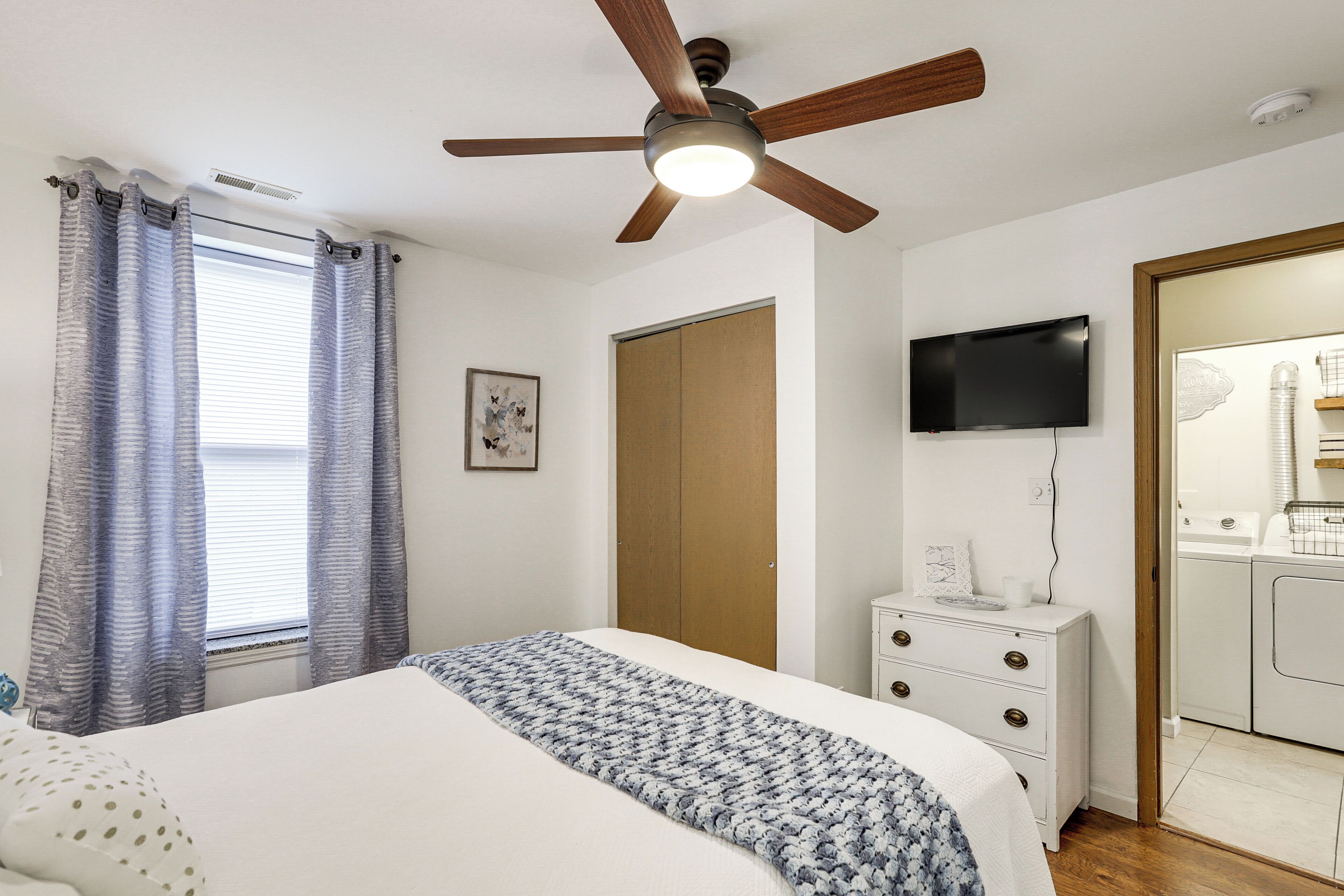 A bedroom with a bed, a ceiling fan, a TV, a wardrobe, and a washing machine.
