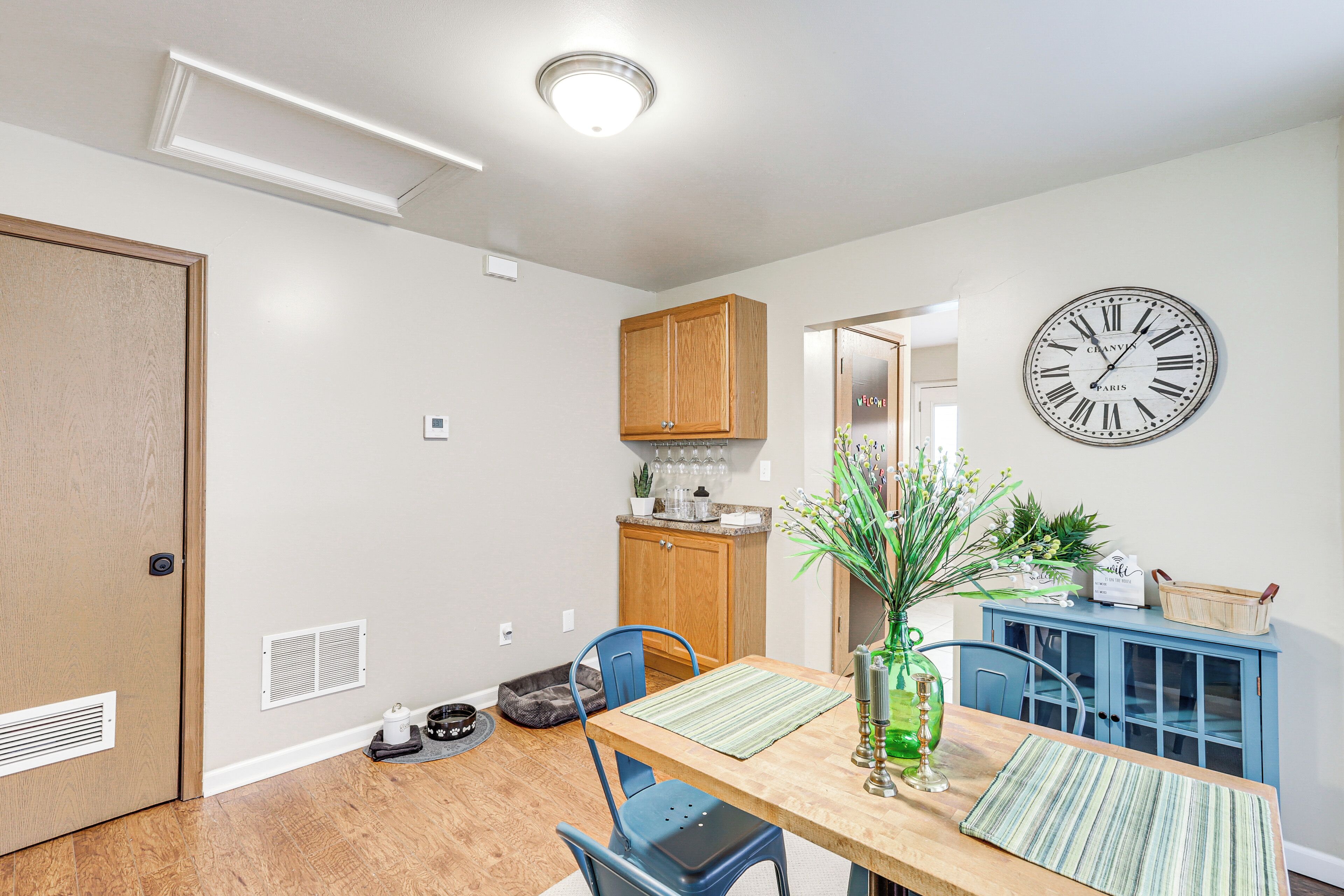 A dining area with a wooden table, chairs, a clock, and a blue cabinet.