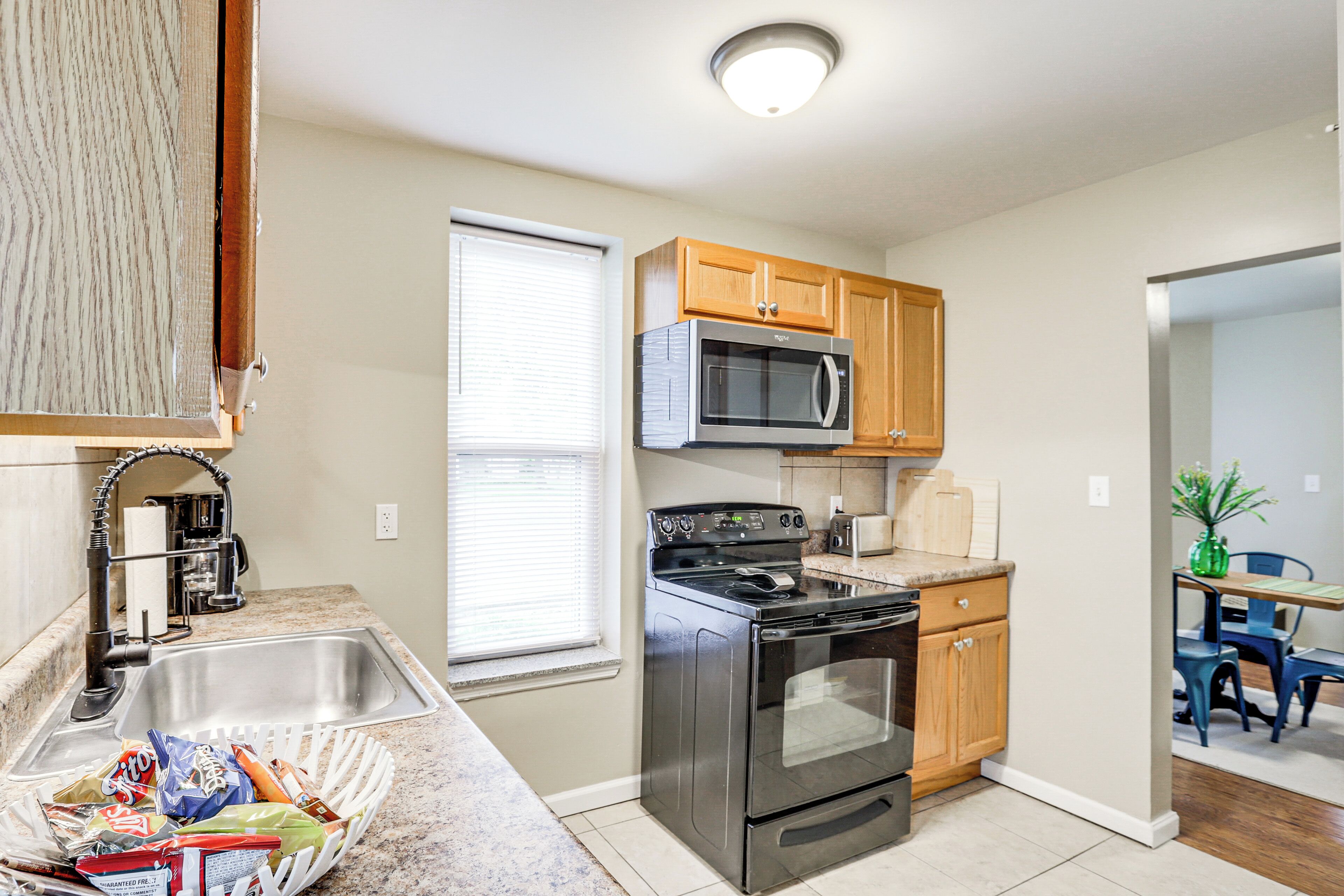 A kitchen with a stainless steel sink, a microwave, an oven, wooden cabinets, and a dining area with a table and chairs.