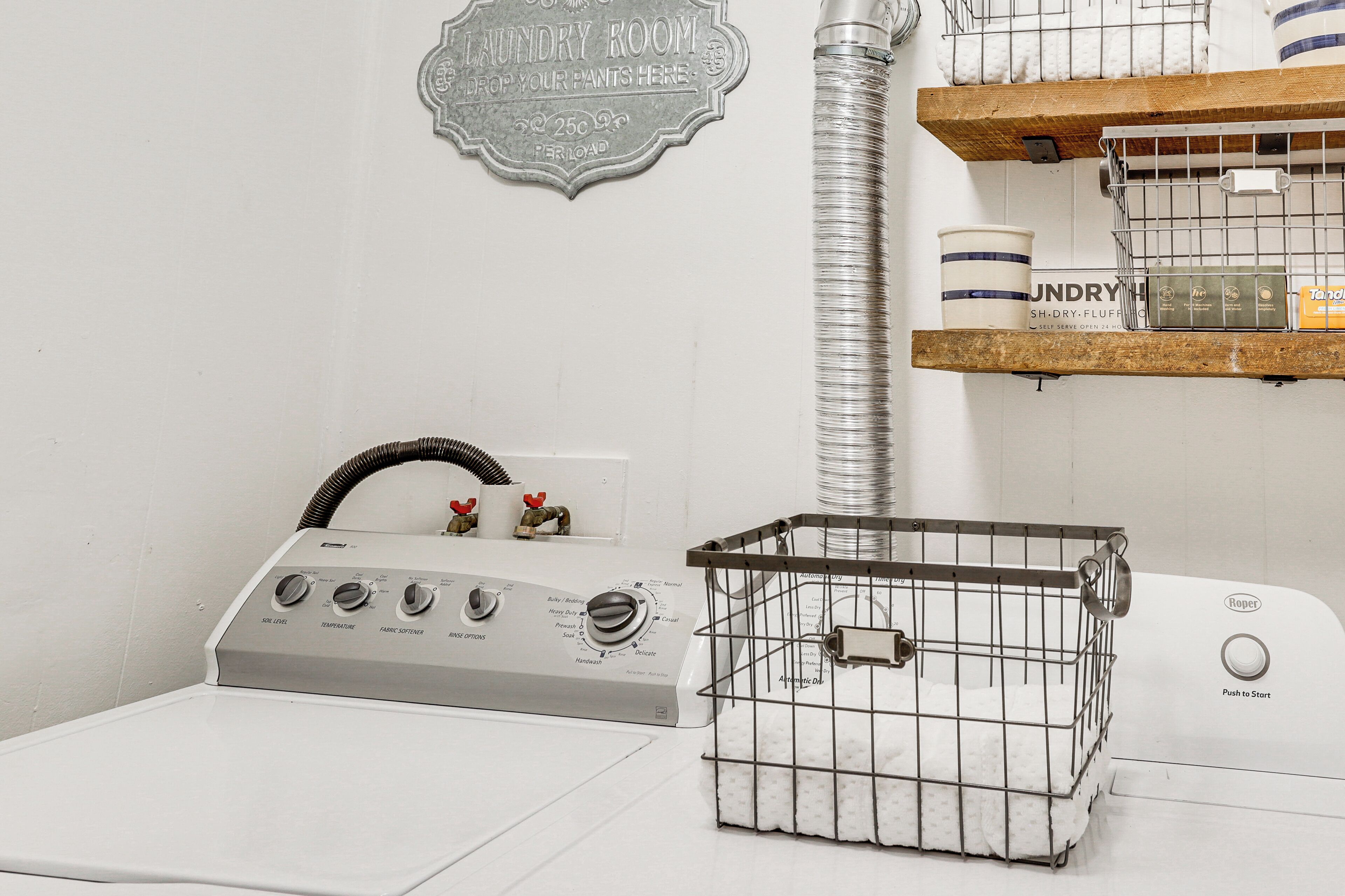 A laundry room with a washing machine, dryer, and a metal laundry basket on the floor.