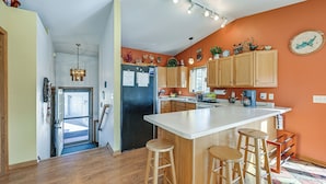 Une cuisine moderne avec des meubles en bois, un grand îlot central doté de tabourets, un réfrigérateur et une horloge murale.