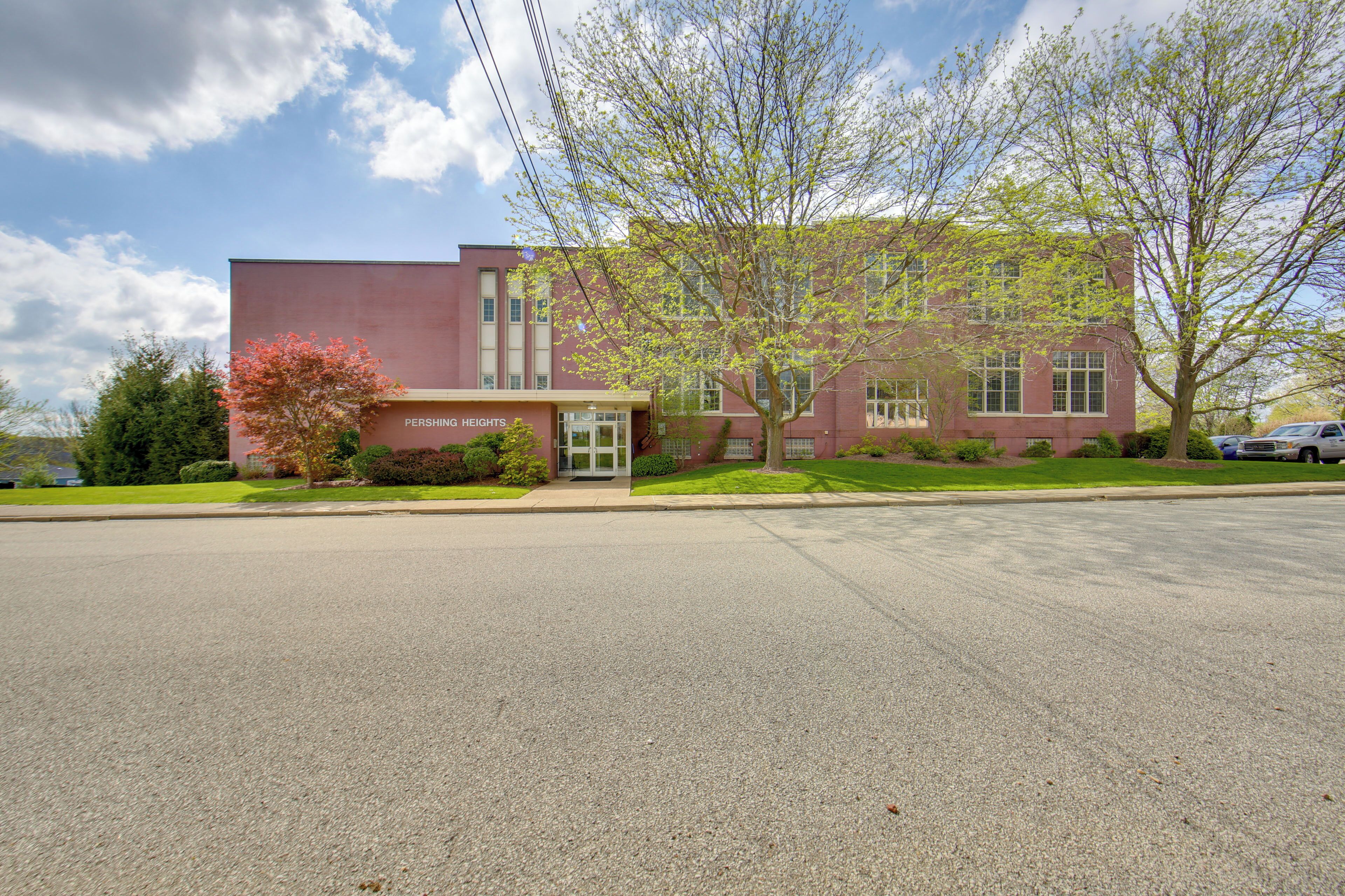 A building with a red brick facade, a sign reading "Pershing Heights," and a parking lot in front.
