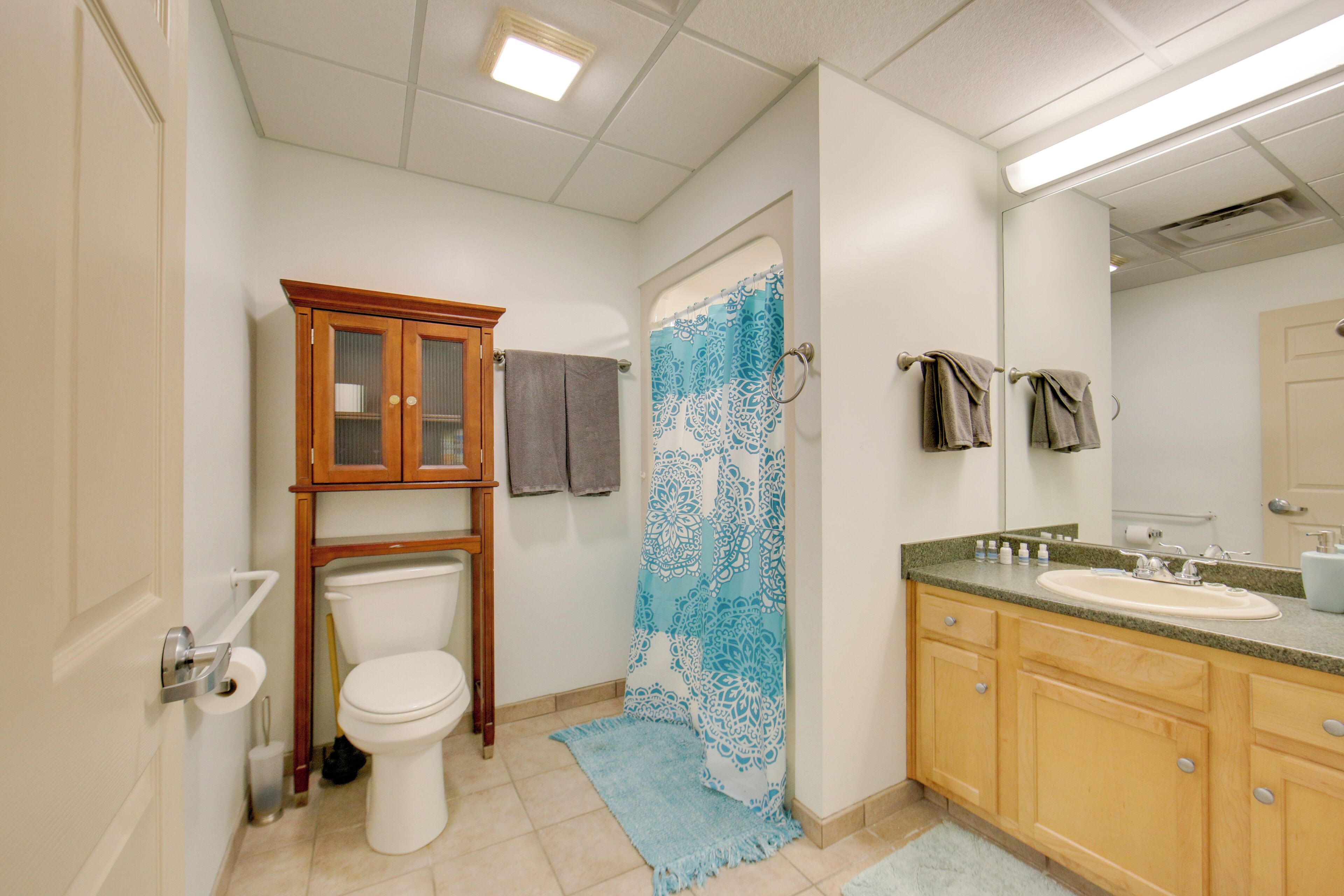 A bathroom with a toilet, a wooden cabinet, a sink, and a mirror.