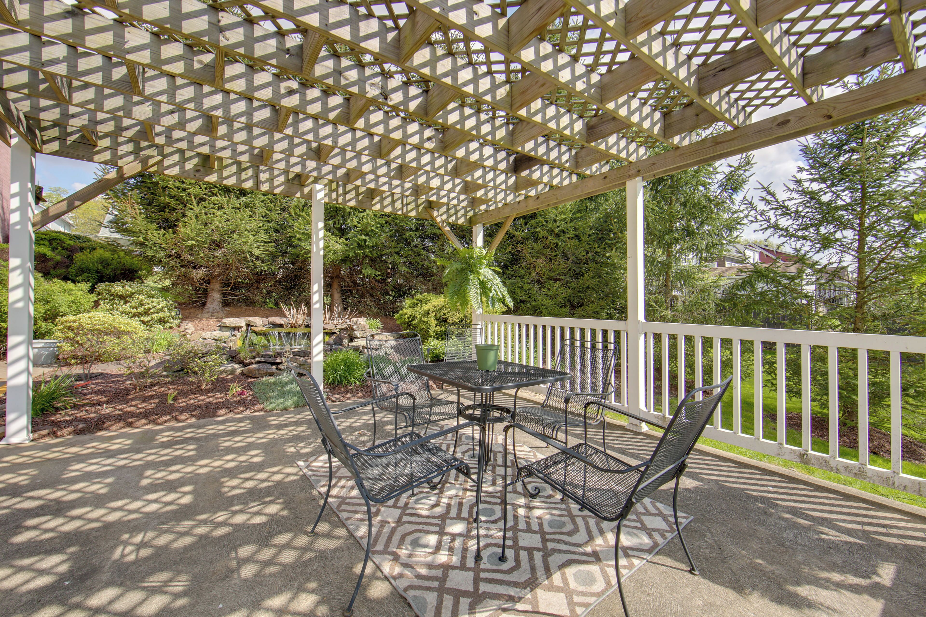 A covered patio area with a table and chairs, surrounded by a white railing and greenery.