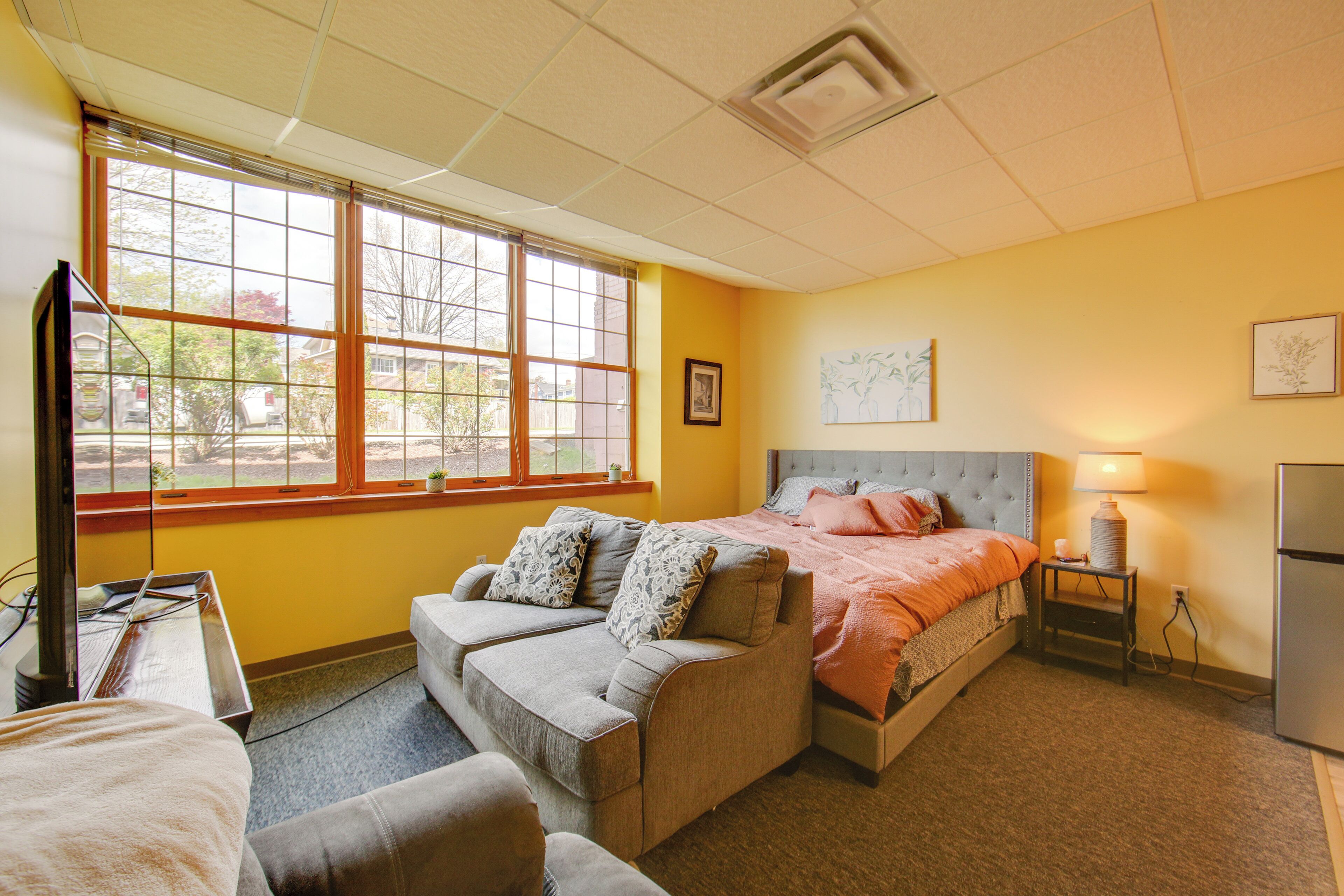A hotel room with a bed, two sofas, a TV, a lamp, and a refrigerator.