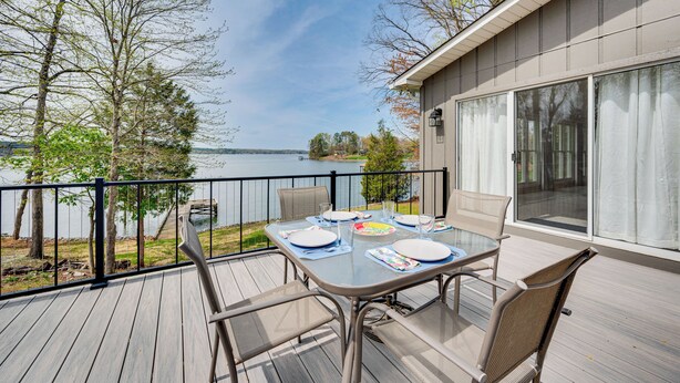 Eine Terrasse mit einem Tisch, gedeckt für vier Personen, mit Blick auf einen See.